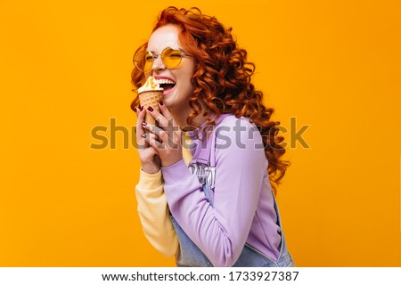Curly cheerful woman in purple sweater and yellow sunglasses eating mango ice cream