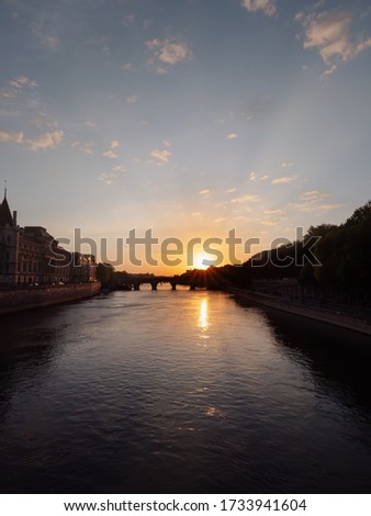 View from the Menial Bridge in Paris amid stunning sunset. The rays of the sun illuminate the palace of justice and are reflected in the Seine.