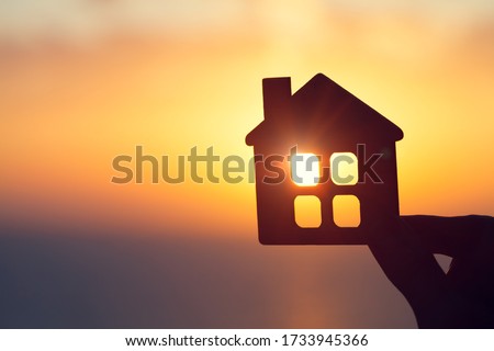 silhouette of man's hand holding small wooden house against sunset or sunrise light, sweet home and family concept, real estate agent offer new house for rent, copy space  Royalty-Free Stock Photo #1733945366