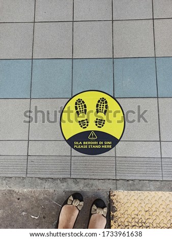 Cut out feet and Sticker on floor tiles with words Please stand here for Social Distancing, Covid -19 prevention