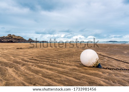 Close-up view of a white buoy and its anchorage chain, lying on the sand on the beach, Brittany, France, under a cloudy sky