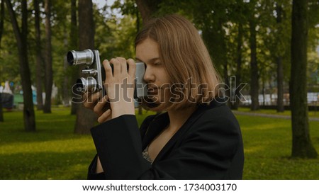 Portrait of a Teenage blonde girl shoots with a vintage movie camera.Against the background of a green park.Close up.