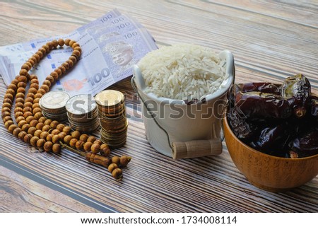 Money , rosary, dates  coin stacked  ,  and rice  on wooden background. Zakat Concept. Zakat is the sharing of wealth from the rich for the less fortunate.