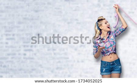 Young happy woman holding telephone tube. Excited pin up girl, profile. Blond model at retro fashion and vintage concept. White brick wall background. Copy space for some slogan, sign or ad text. 