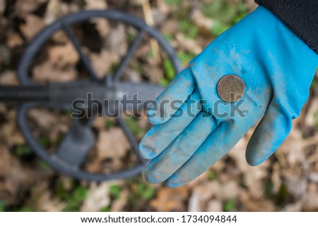 Found old valuable ancient coin in the digger's hand against the background of a metal detector. A rubber-gloved digger 
archaeologist found an expensive 
historical coin in the forest