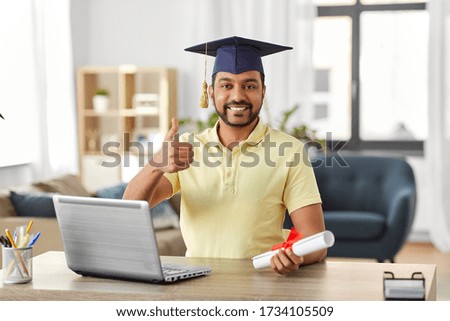 e-learning, education and people concept - happy smiling indian male graduate student with laptop computer and diploma showing thumbs up at home