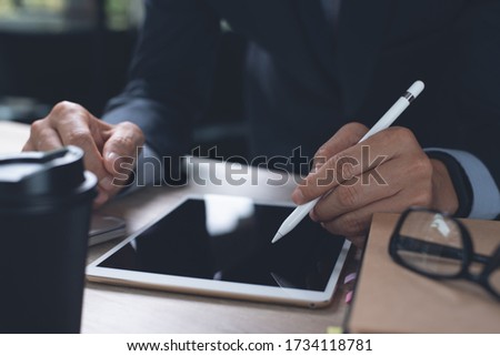 Businessman hand working with stylus pen on digital tablet, laptop computer on desk in modern office, close up. Man messaging on tablet pc via mobile apps. Business plan, electronic signature concept