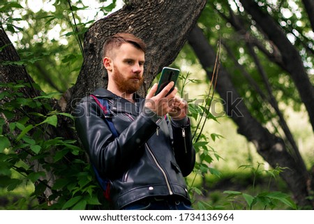 lay down on a tree branch and looks at the smartphone screen in the middle of a green forest.