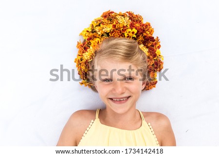 Close up portrait of 9 year old lovely teen girl lying against white background with hair adorned with yellow and orange marigold flowers shot from birds perspective