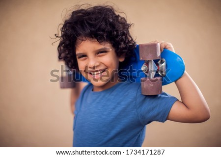 A portrait of happy kid boy with curly hair holding skateboard. Children,leisure and lifestyle concept