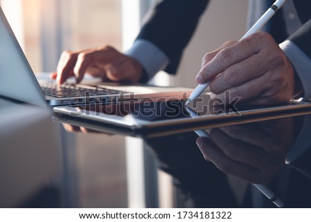 Businessman hand using stylus pen signing contract on digital tablet while working on laptop computer in modern office, electronic signature. Business man taking note on touchpad, business concept