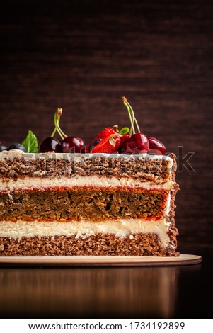 Chocolate sponge cake with white cream and berries, strawberries, cherries and mint. Cake cutaway on cinnamon background. copy space