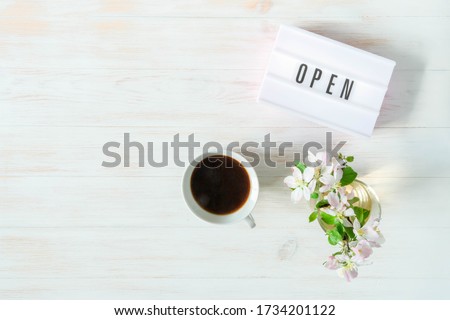 Word OPEN displayed on lightbox, coffee cup and vase with blossoms on wooden table. Opening after quarantine concept. Freedom after self-isolation. Seasonal end of coronavirus pandemic. Vintage mockup