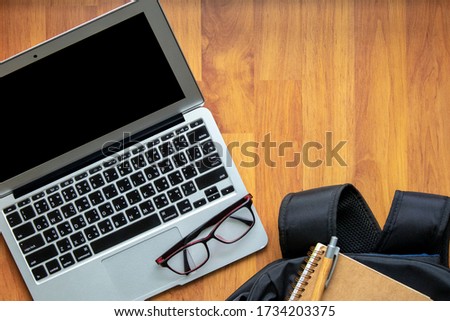 Work space with a laptop. There are a glasses on touch pad. A book and a pen is on a backpack. There are space for text on wood floor. Work from home, online meeting concept.