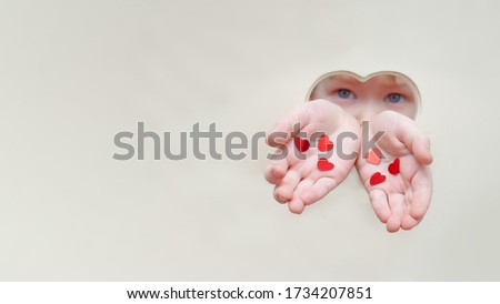 Hands and face of a baby from a hole in the shape of a heart. Childrens hands hold out hearts and give love. Unconditional love and affection, concept of childrens love, mothers day, adopted child