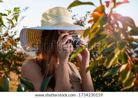 Side view of a girl with a hat taking photos with a retro camera in the park