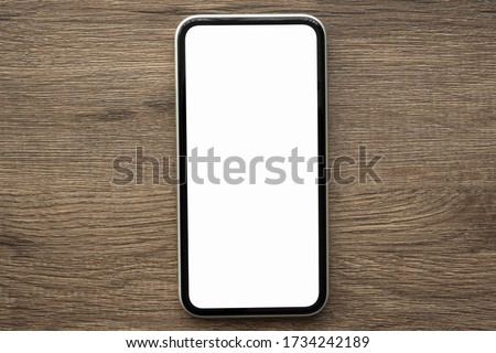 Smartphone with blank mock up screen is on top of wood table. Top view, flat lay.