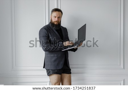 A bearded man in a jacket and without pants works at home in isolation. home Office