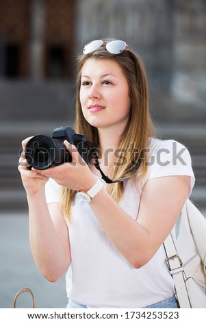 Portrait of young cheerful woman looking curious and taking pictures outdoors