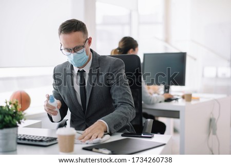 Businessman disinfecting desk in the office. Covid-19 concept. 