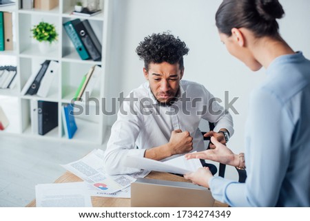 Selective focus of businesswoman pointing at papers near offended african american man at table in office