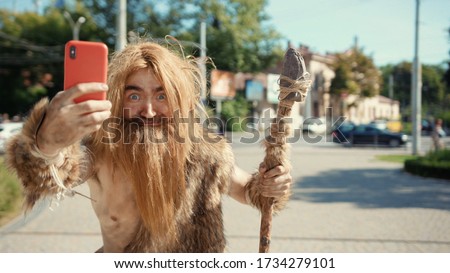 Prehistoric tribesman of neanderthals noticing somebody hurrying taking photographs like paparazzi on future smartphone in modern civilization city.