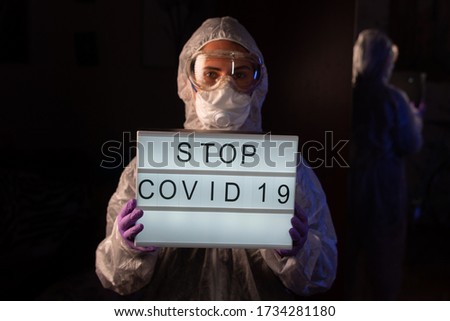 Doctor, virologist, scientist, man wearing chemical protection suit, respirator holding lightbox with sign stop coronavirus.