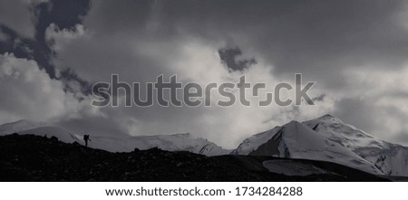 Scenic landscape of snowy mountain peak. Cloudy sky. Shadow silhouette of a man. Expedition.
