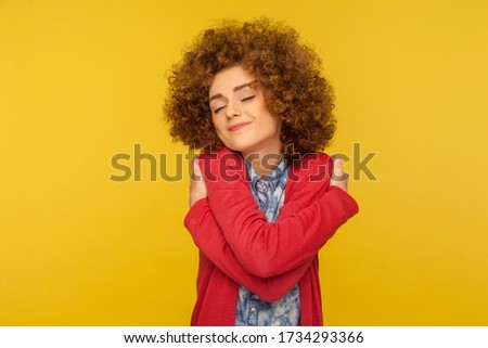 I am the best! Portrait of selfish woman with fluffy curly hair embracing herself and smiling with pleasure expression, self-loving and egoism concept. indoor studio shot isolated on yellow background Royalty-Free Stock Photo #1734293366