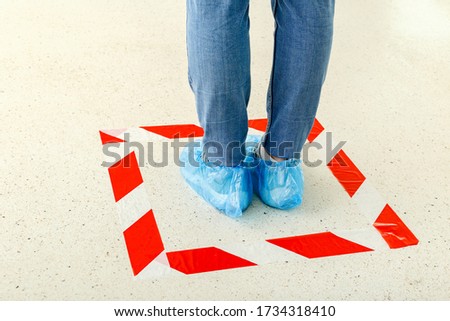 Woman stand in line keeping social distance wearing overshoes, medical shoe covers in Store, supermarket, hospital. People standing behind a warning line during covid 19 coronavirus. Social distancing