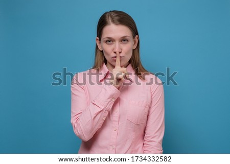 Young woman holding a finger on her lips showing silent gesture. Studio shot on blue wall