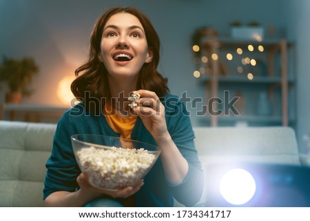 Young woman watching projector, TV, movies with popcorn in the evening. Girl spending time at home. Royalty-Free Stock Photo #1734341717