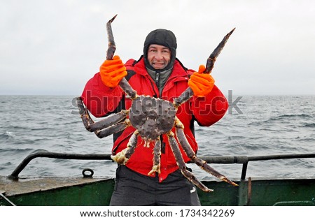 Happy fisherman in a red jacket caught and holds in his hands a beautiful huge red king crab against the backdrop of the cold North Sea, Barents sea Royalty-Free Stock Photo #1734342269