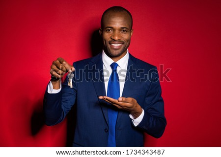 Photo of handsome dark skin business guy confident worker hold open arm offer sale price demonstrating keys chain wear formalwear suit tuxedo isolated burgundy red background