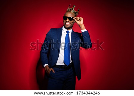 Photo of handsome selfish cool dark skin business guy bossy person golden diadem on head looking flirty eyes wear sun specs formalwear suit tuxedo isolated burgundy red background