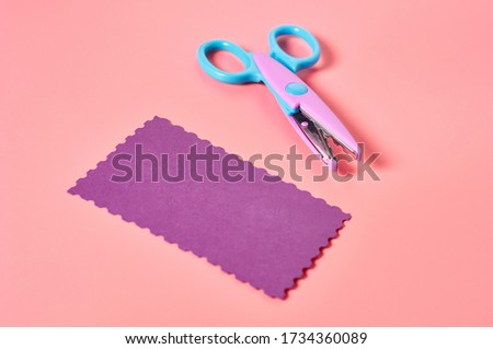 Scissors for decorative curly cutting and blank paper for craft with wave border on pink background. Concept of handmade, leisure or preschool education