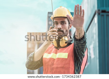 Caucasian beard foreman wearing safety helmet and making hand to stop while talking on walkie talky