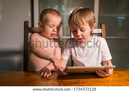 Portrait of brother and sister using digital tablet at the table in the kitchen and watching cartoons. Portrait of a smart pre-school child using devices.