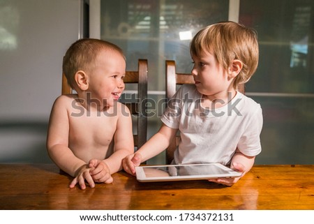 Portrait of brother and sister using digital tablet at the table in the kitchen and watching cartoons. Portrait of a smart pre-school child using devices.