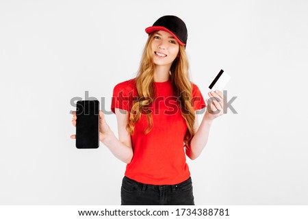 Courier girl in uniform, using a mobile phone and holding a credit card on a white background. Delivery, payment by Bank transfer,