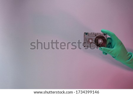 Green Hand holding audio cassette tape in the color light. Beautiful minimal in neon light. Minimalism retro style concept. Background pattern for design. 