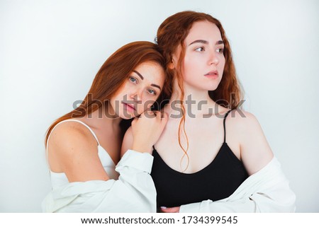 portrait of two redheaded young women one puts her head tenderly on the other's shoulder standing on isolated white backgroung, beauty and style concept