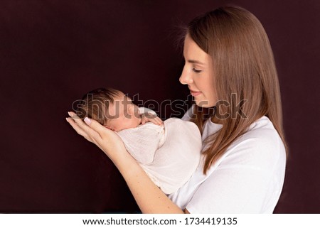 Close up portrait of a happy young mother hugs and kisses her cute charming newborn baby.