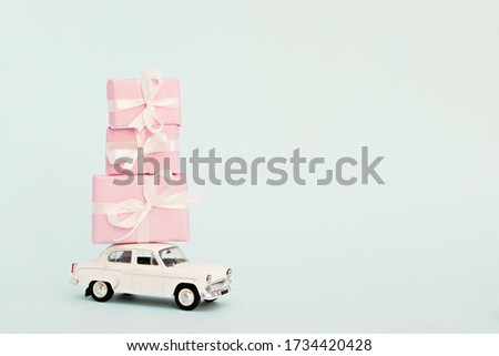 White retro toy car on a blue background with pink gifts.