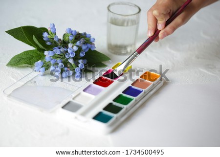children's hand soaks a brush in watercolor paints, on a light table.
