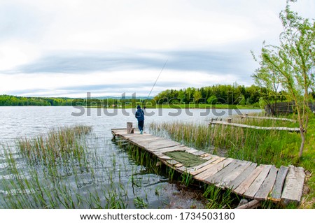 fishing pole with beautiful lake, mountains, forest and steel sky background. Fishing tool and sport concept