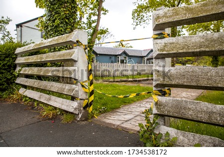 Image of a white picket fence made from triangles with yellow and black tape tied to the fence blocking anybody from entering the pub car park or beer garden due to government issued lockdown 