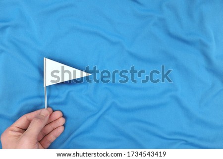 Hand holding a white flag in blue background. Peace, ceasefire, surrender and truce concept.