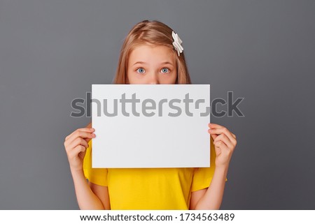 teen girl in yellow t-shirt holding empty white paper close-up, space for text, copy space
