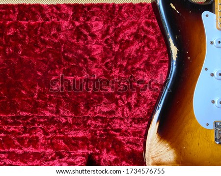 vintage sunburst electric guitar, made of alder wood, with relic  and scratches on his body Leaning in a tweed patterned case with a red carpet There is a space in which to put text for your business.